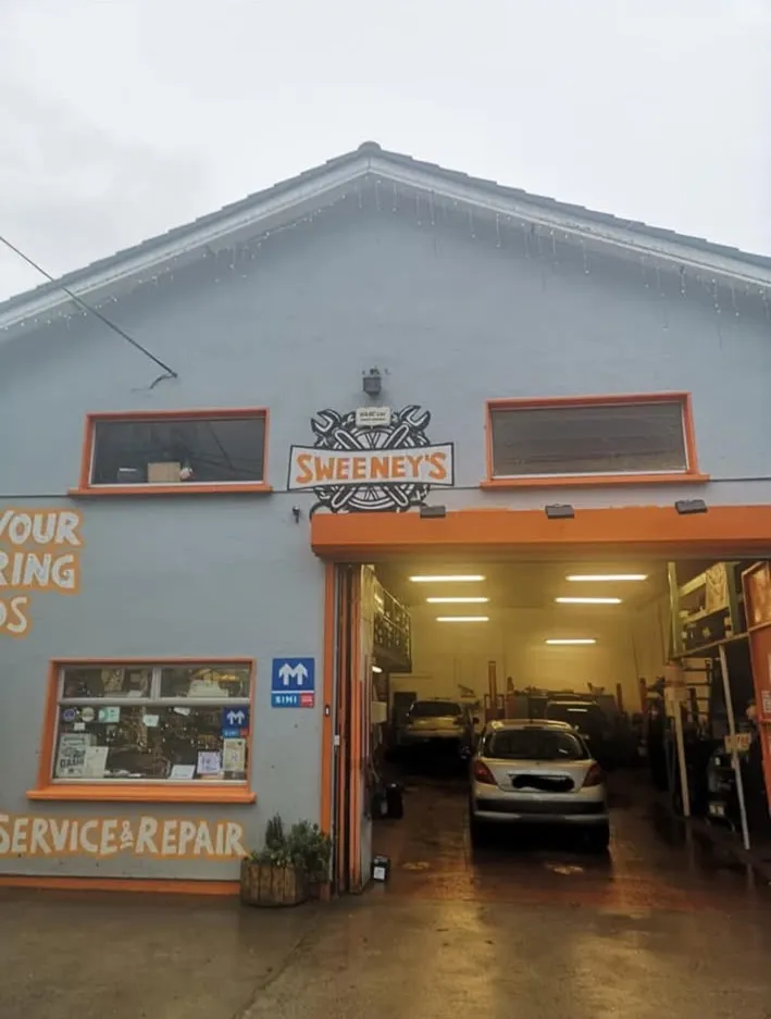 Exterior of Sweeney's Garage with the orange Sweeney's sign above the open workshop door